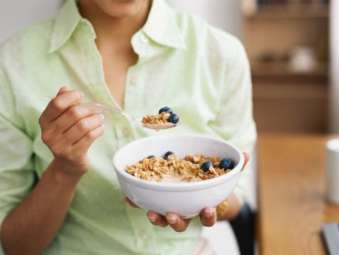 Woman holding bowl of cereal, mid section, close-up